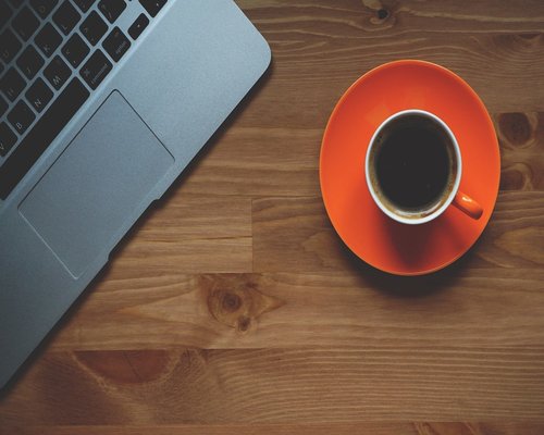cup of coffee and fresh snacks next to a laptop on a desk